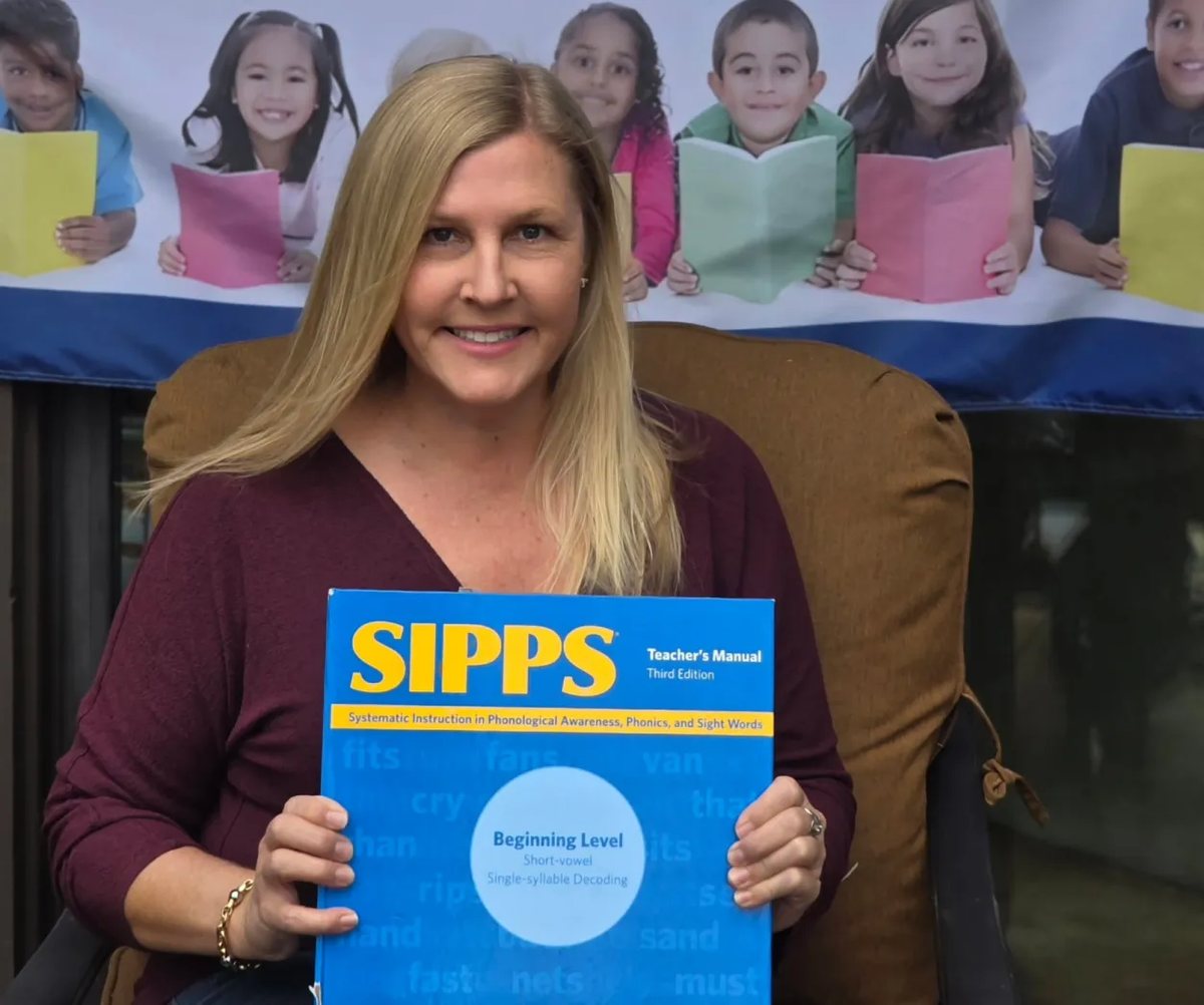 Sarah holding a SIPPS Teacher's Manual in front of the Young Reader Support banner