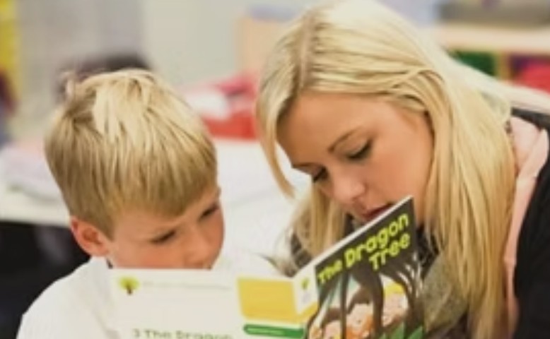 A teacher and a young boy reading a book together